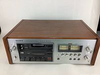 Front view of Sony stereo cassette deck showing wooden case and stainless steel front panel with control knobs, cassette slot, and VU meters.