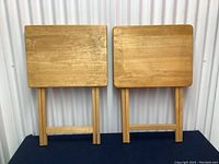 Two vintage wooden TV tables folded with legs visible, showing solid wood construction and wear
