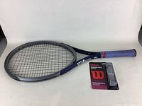 Wilson Triad tennis racket displayed flat with blue grip tape showing, accompanied by new spare grip in packaging