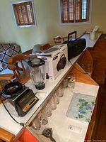 Osterizer blender with glass jar and black base next to its box and several glass cups on the counter