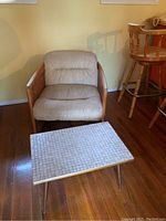 Photo showing cane club chair with beige cushions and metal side table in front on hardwood floor.