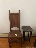 Antique wooden Victorian style chair with carved vertical panel backrest and turned front legs with detailed crossbar. Wooden side table with square top featuring etched floral design and a lower shelf, both supported by curved legs.