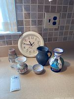 Photo showing six ceramic hand painted vases of various sizes and shapes alongside a white Westclox wall clock.