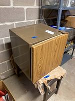 Closed Kenmore mini fridge showing wood veneer door, metal body sides, resting on worn wooden bench.