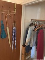 Photo showing women's jackets and scarves hanging on a closet rod next to the door with the umbrellas.
