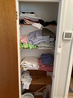 Closet shelves with various folded linens including sheets, pillowcases, towels, and washcloths in multiple colors.