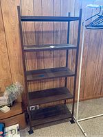 Full view of metal shelving unit with wood-finish shelves against wood panel wall.