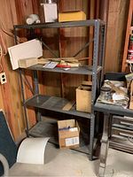 Metal shelving unit in basement with four shelves and miscellaneous items around. Shelf is empty of contents to be sold.