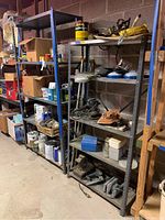 Photo of two heavy-duty metal shelving units standing side by side in a garage or workshop space, showing five shelves each filled with various tools and materials which are not included.