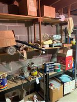Overview of basement shelves with painting supplies including containers, tools, paint pans, brushes, boxes.