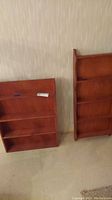 Two wooden display shelves leaning against a wall on a tiled floor.