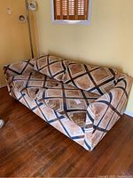 Front angle view of the patterned pull-out fabric sofa bed with removable cushions against beige wall on wooden floor.