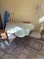 Round table with yellow plaid formica top and four chairs with light wood seats and backs with metal cantilever frames, set on tiled floor with yellow plaid wallpaper.