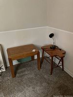 Two wooden side and end tables placed against a wall; the smaller uniquely shaped table holds a black table lamp with wired cord.