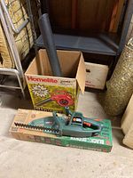 Black & Decker electric hedge trimmer on top of its original box and next to a Homelite blower box with blower tube.