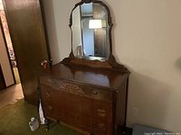 Full view of antique wooden dresser with attached mirror showing carved details and brass drawer handles.