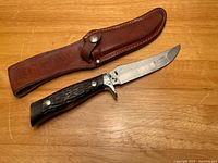 Camillus fixed blade knife with stag grip handle and leather sheath laid on wooden surface.