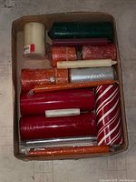 Box of assorted candles viewed from above on a wooden floor. Shows variety of colors and types packed loosely in a box.