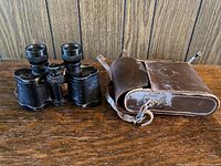 Photo of binoculars and leather case placed on wooden surface