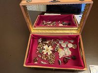 Wooden jewelry box open with assorted vintage and designer costume jewelry inside on red fabric lining. Box lid has mirror.