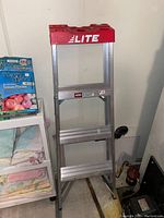 Side view showing the full ladder with three grooved metal steps and red top.