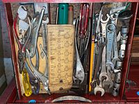 Top view showing assortment of hand tools including pliers, gauge tool, screwdrivers, and wrenches in metal tray.