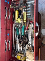 Top view of open red metal toolbox drawer containing assorted vintage hand tools including screwdrivers, pliers, wrenches, socket sets, and a pressure gauge.