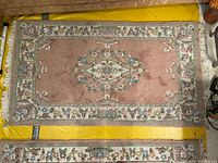 Full view of one vintage rug with floral medallion and vine border in pink and pastel colors, laid flat.
