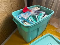 Overview of turquoise plastic storage bin filled with assorted holiday decorations and fabrics.