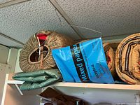 Photo showing rolled and folded sleeping bags and tarps stacked on shelf, including brown, patterned, and green items.