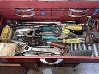 Drawer view showing assortment of aged hand tools including wrenches, pliers, pressure gauge, and screwdrivers.