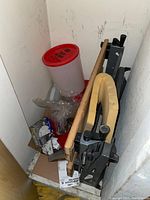 Workbench, folded plywood or wood panels with metal frame and a large red-lid plastic container, small boxed items scattered around.