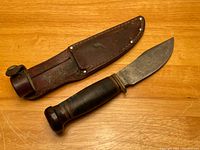 Photo of knife with leather sheath laid on wooden surface
