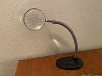 Full view of vintage standing magnifying glass tool showing flexible neck and cast iron base on wooden surface.