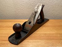 Full view of Stanley wood planer showing cast iron body, wooden front knob and rear handle, and metal blade assembly with Stanley logo.