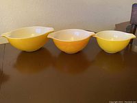 Three Pyrex mixing bowls in yellow and orange colors side by side on a brown surface