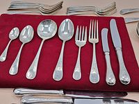 Close-up image of various flatware pieces laid out on a red cloth including spoons, forks, knives, and serving spoons
