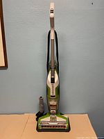 Front view of Bissell multi-surface floor cleaner upright vacuum with brush attachment standing next to it and placed on a black plastic base.
