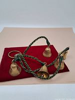 Six brass bells arranged on a flat surface showing the full set with the braided cord and loop for hanging.