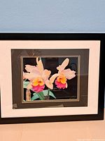 Full view of framed photograph showing two orchids with black frame and white/brown matting.