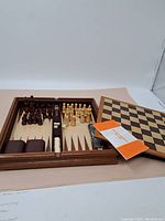 Wooden chess and backgammon board with chess pieces arranged inside and a separate chess/checkered board beside it.