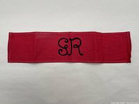 Full view of the red armband showing the rectangular shape and centered black embroidered 'GR' letters.