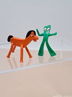 Gumby and Pokey figurines displayed on clear surface, showing full figure details.