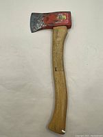 Front view of the hatchet showing red painted metal head and curved wooden handle with natural finish.