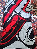Full view of scarf laid flat showing large bold indigenous style pattern in red, black, and white colors on a vintage carpet background.