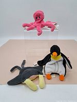 Lot with 3 Ty Beanie Babies plush toys: pink octopus on clear display stand, black and white penguin with orange feet and beak, and gray walrus with tusks on beige surface.
