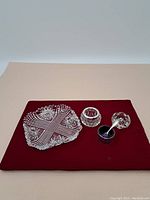 Overview of the lot showing the clear crystal divided dish, two small clear crystal bowls, cobalt blue glass dish with silver holder, and small silver spoon on a red cloth.