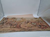 Full view of the tapestry laid flat showing the entire woven scene of figures, camels, tents, and palm trees with fringed edges.