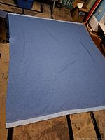 Full view of the blue Ayerspun wool blanket laid out flat on a carpeted floor.