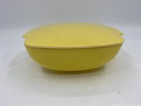 Side view of the vintage yellow Pyrex ovenware dish with lid on, showing the rounded shape and handle extensions.